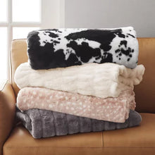 Stack of folded luxury faux fur throw blanket in cow print, cream, pink dot and gray on leather sofa