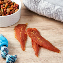 Golden Rewards chicken jerky dog treats next to a bowl of dry kibble and a blue chew toy on wooden floor